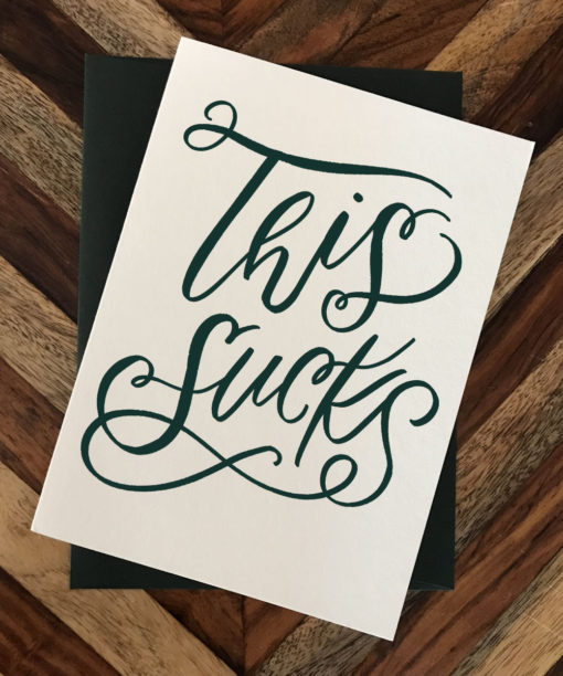 Photo of card that reads "This Sucks" sitting on wooden surface