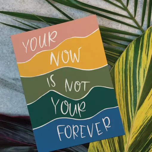 Photo of card on leaves. The card reads "Your now is not your forever" in colored stripes and white text.
