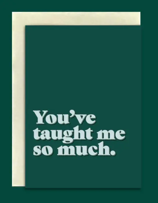 Close-up product image of a greeting card in front of a cream envelope. The card is a dark green. Bold, light green text at the bottom reads, "You've taught me so much."