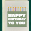 close up of the front of a closed greeting card lying on top of a green envelope. The card features a large, sage green rectangle, presented to look like a cake. The rectangle is topped with multicolored, lit candle shapes. The cake reads "Happy Birthday to You" in white text
