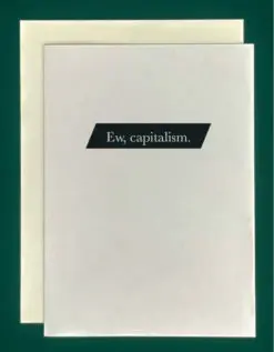 Close-up of a white greeting card on top of a cream-colored envelope, all on a forest background. The card features a small, black, angled rectangle. Inside are the words, "ew, capitalism." in white text.