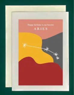 Close-up of a white greeting card on top of a cream-colored envelope, all on a forest background. The card features the constellation Aries superimposed on abstract blobs of different colors - dark red, goldenrod, gray, and pink. Text at the top of the greeting card reads, "Happy Birthday to my favorite Aries"