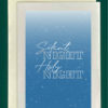 Close-up of a white greeting card on top of a cream-colored envelope, all on a forest background. The card design is a blue night sky with the words Silent Night Holy Night in cursive font.